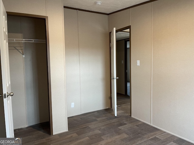 unfurnished bedroom with a textured ceiling, ornamental molding, dark wood-style flooring, and a decorative wall