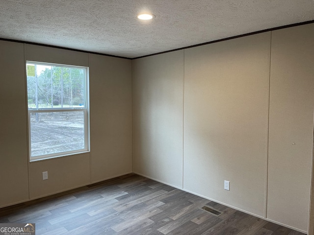 unfurnished room with crown molding, a textured ceiling, visible vents, and wood finished floors