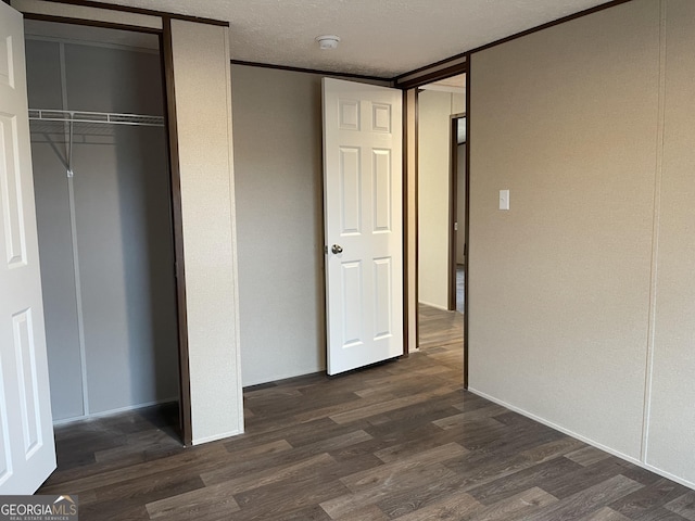 unfurnished bedroom with dark wood-style floors, a textured ceiling, and a closet