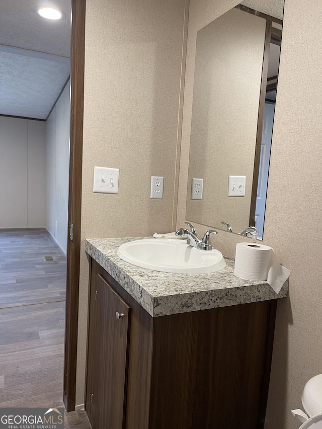 half bathroom with a textured wall, wood finished floors, and vanity