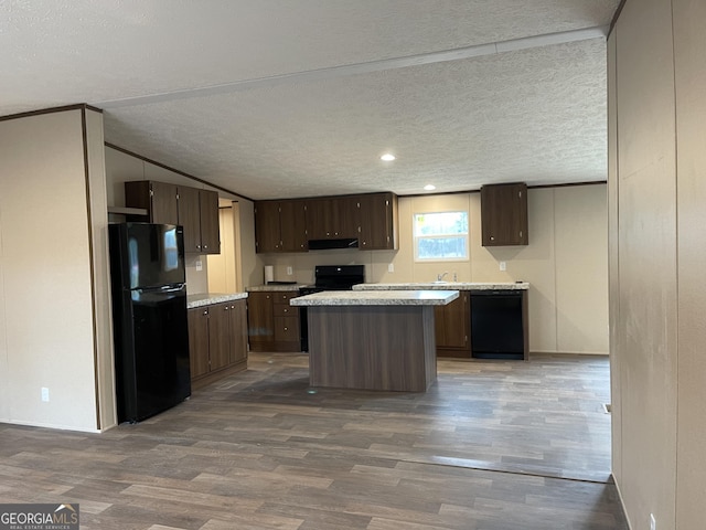 kitchen featuring light countertops, a textured ceiling, wood finished floors, under cabinet range hood, and black appliances