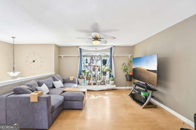 living area with wood finished floors, a ceiling fan, and baseboards