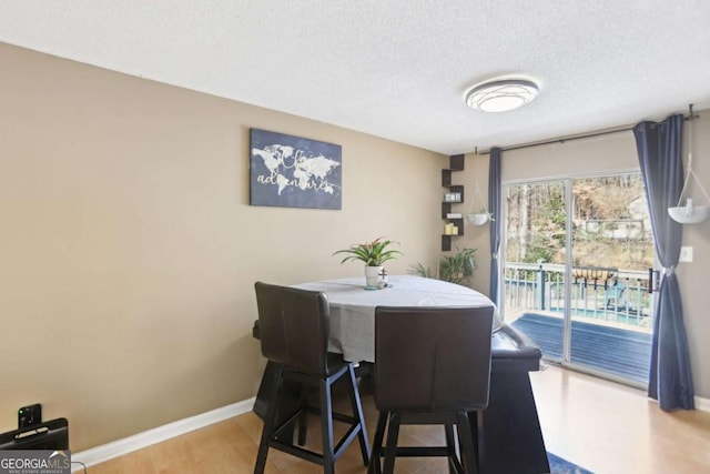 dining area with a textured ceiling, baseboards, and wood finished floors