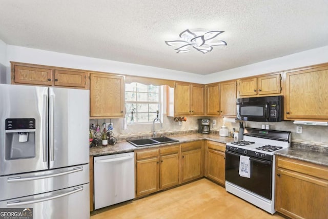 kitchen featuring a textured ceiling, stainless steel appliances, a sink, brown cabinetry, and dark countertops