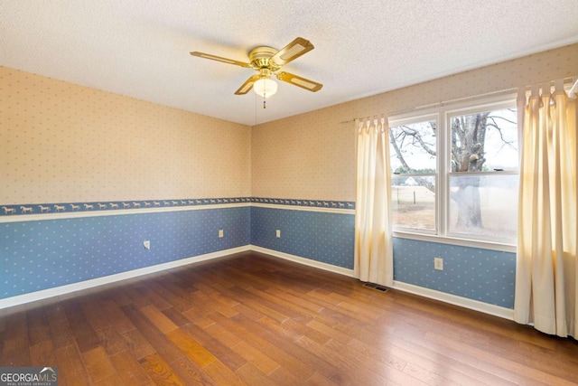 empty room with a textured ceiling, visible vents, baseboards, hardwood / wood-style floors, and wallpapered walls