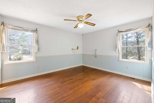 empty room with a textured ceiling, hardwood / wood-style flooring, visible vents, and baseboards