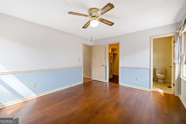 unfurnished bedroom with a walk in closet, a closet, ensuite bath, baseboards, and hardwood / wood-style flooring