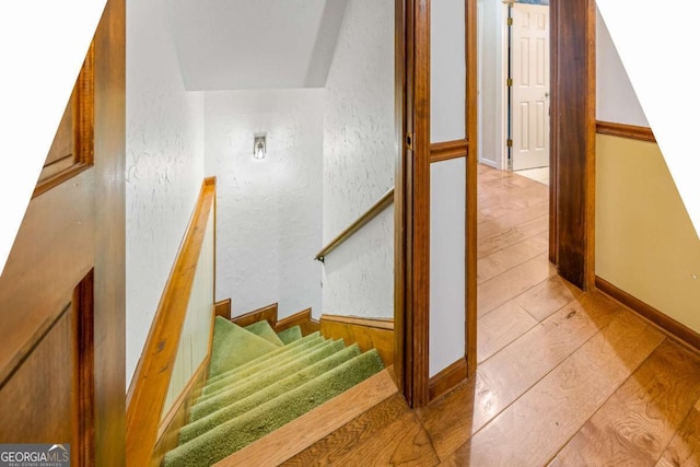 stairway with a textured wall, wood finished floors, and baseboards