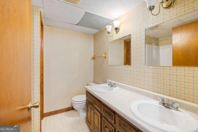 bathroom with double vanity, a drop ceiling, a sink, and toilet