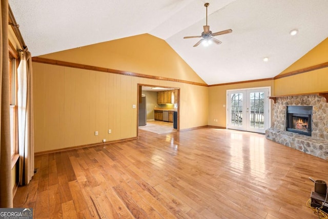 unfurnished living room with ceiling fan, a fireplace, vaulted ceiling, french doors, and light wood finished floors