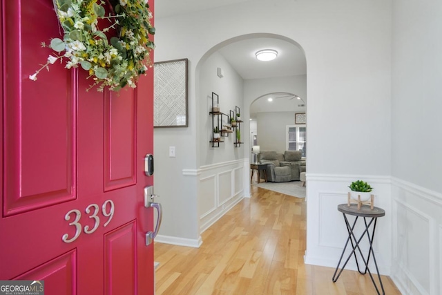 entryway with light wood-style floors, arched walkways, a decorative wall, and a wainscoted wall