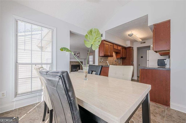 dining area featuring a textured ceiling, lofted ceiling, a tile fireplace, visible vents, and baseboards