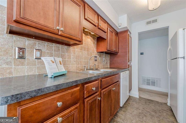 kitchen featuring dark countertops, visible vents, brown cabinetry, a sink, and white appliances