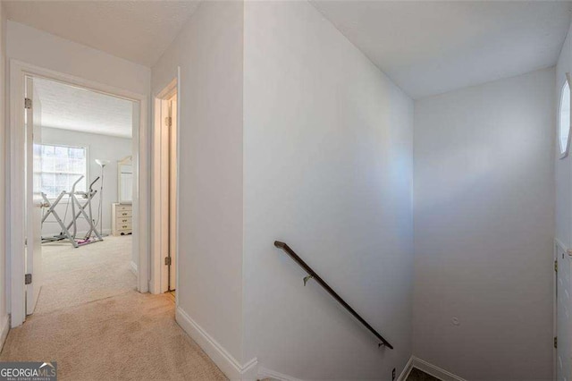 hall with baseboards, light colored carpet, and an upstairs landing