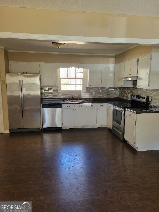 kitchen with stainless steel appliances, backsplash, dark countertops, and a sink