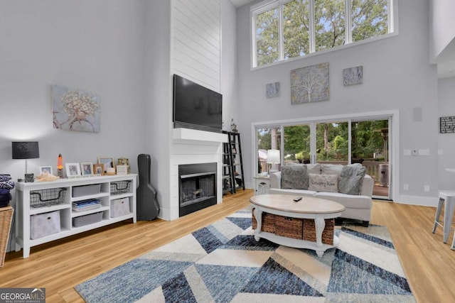 living room featuring a fireplace, a towering ceiling, baseboards, and wood finished floors