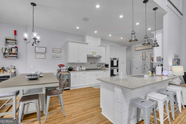 kitchen with stainless steel double oven, white cabinets, a sink, and light wood-style flooring