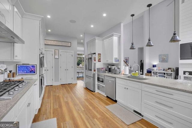 kitchen featuring light wood-style flooring, stainless steel appliances, wall chimney range hood, white cabinetry, and a sink