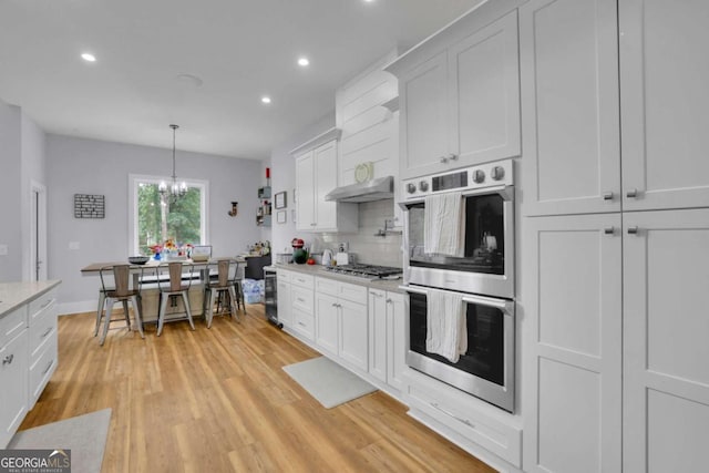 kitchen with a chandelier, white cabinets, appliances with stainless steel finishes, light wood-type flooring, and decorative backsplash