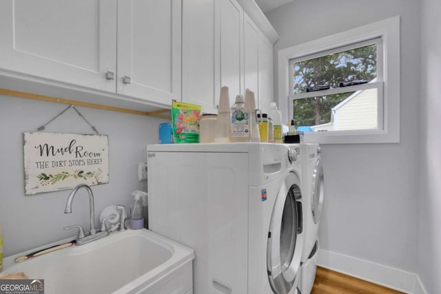 laundry area featuring cabinet space, baseboards, wood finished floors, independent washer and dryer, and a sink