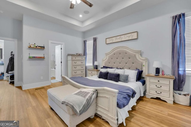 bedroom with connected bathroom, recessed lighting, baseboards, light wood finished floors, and a raised ceiling