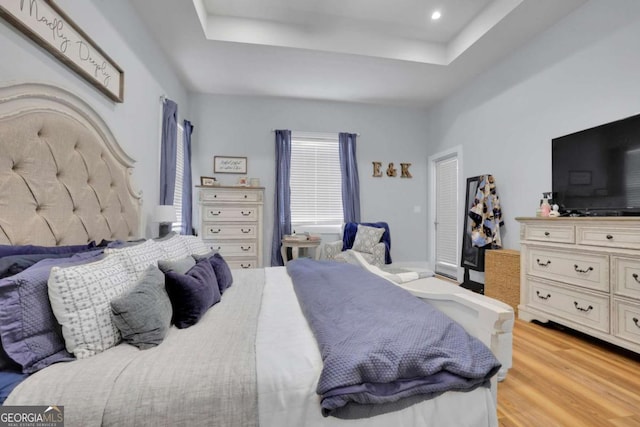 bedroom with light wood-style floors and a raised ceiling