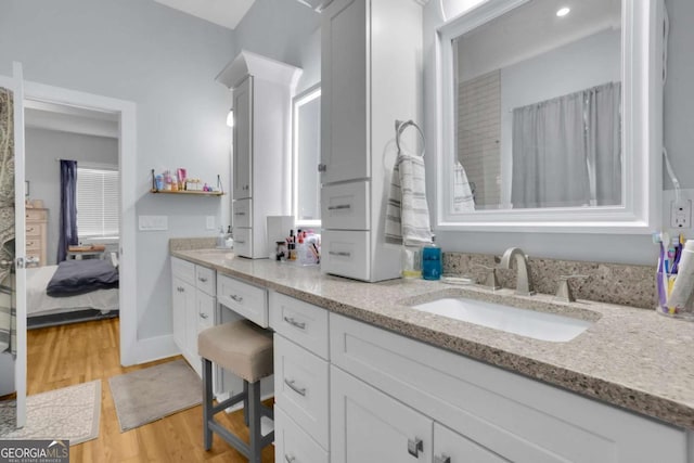 bathroom with ensuite bathroom, wood finished floors, a sink, baseboards, and double vanity