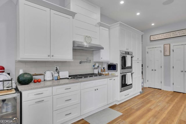 kitchen featuring beverage cooler, white cabinets, light wood-style flooring, appliances with stainless steel finishes, and backsplash