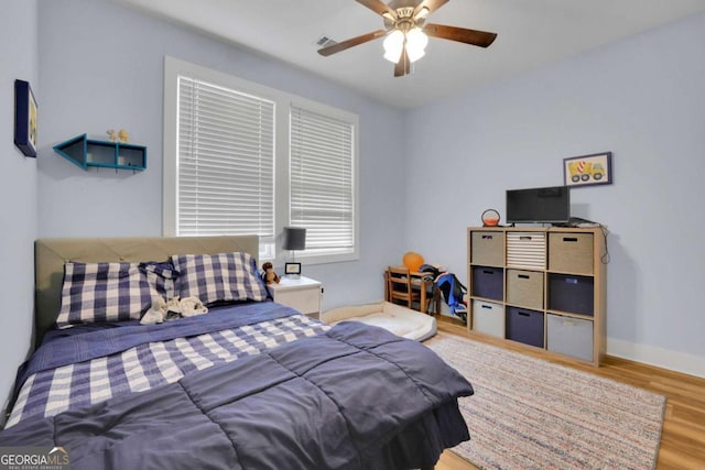 bedroom with a ceiling fan, wood finished floors, visible vents, and baseboards