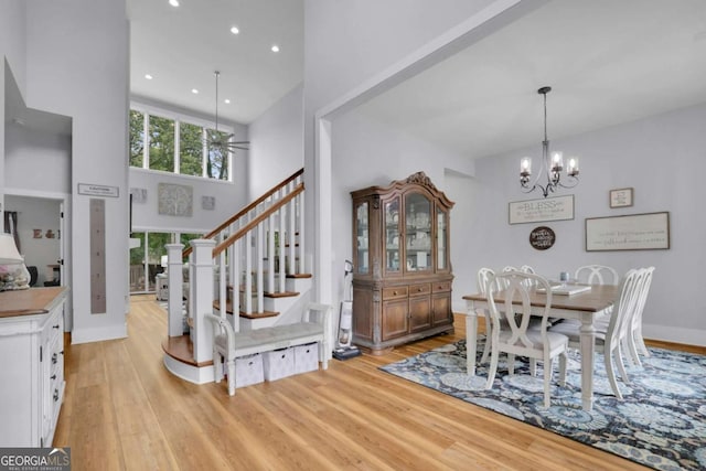 dining room with a towering ceiling, light wood-style floors, stairway, and an inviting chandelier