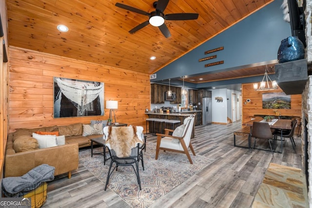 living area with lofted ceiling, wooden ceiling, light wood-style flooring, ceiling fan with notable chandelier, and wood walls