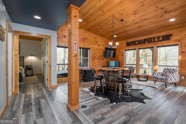 dining space with lofted ceiling, wood walls, wood finished floors, and decorative columns