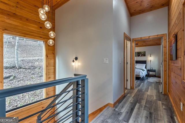 hall featuring wooden walls, baseboards, wooden ceiling, hardwood / wood-style flooring, and high vaulted ceiling