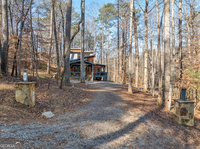 view of front facade featuring gravel driveway, a forest view, and a porch