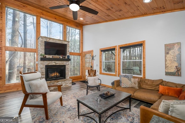 living area featuring a stone fireplace, wood finished floors, wood ceiling, and a healthy amount of sunlight