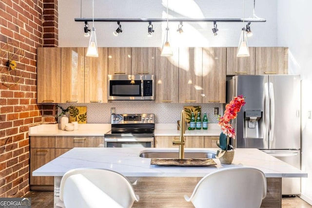 kitchen featuring hanging light fixtures, brick wall, stainless steel appliances, and a sink