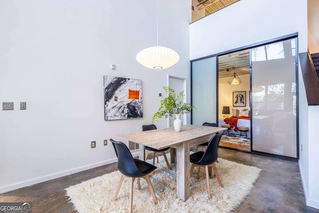 dining space with finished concrete flooring, a high ceiling, and baseboards