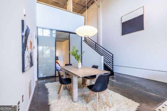 dining room with concrete flooring, visible vents, a towering ceiling, and stairs