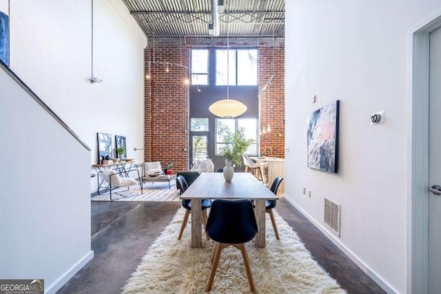 dining room with finished concrete flooring, a high ceiling, visible vents, and baseboards