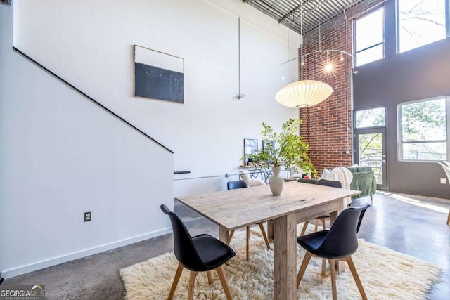 dining room featuring finished concrete flooring, a high ceiling, and baseboards