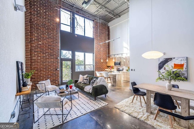 living area with finished concrete flooring, brick wall, and a towering ceiling