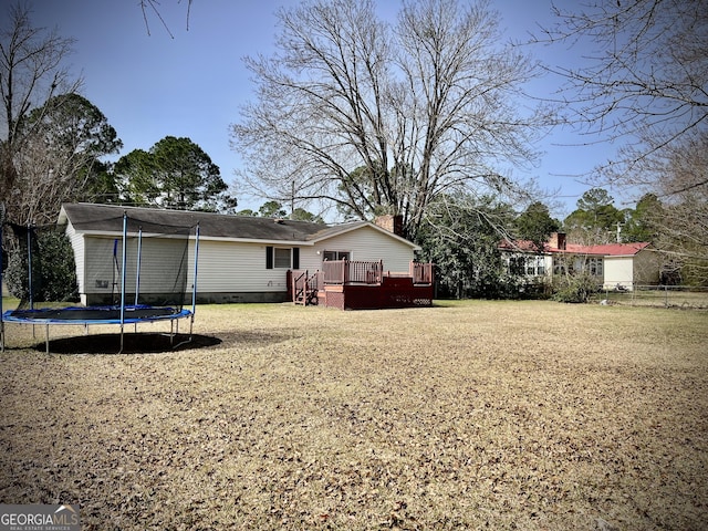 back of property with a lawn, a chimney, a trampoline, fence, and a deck