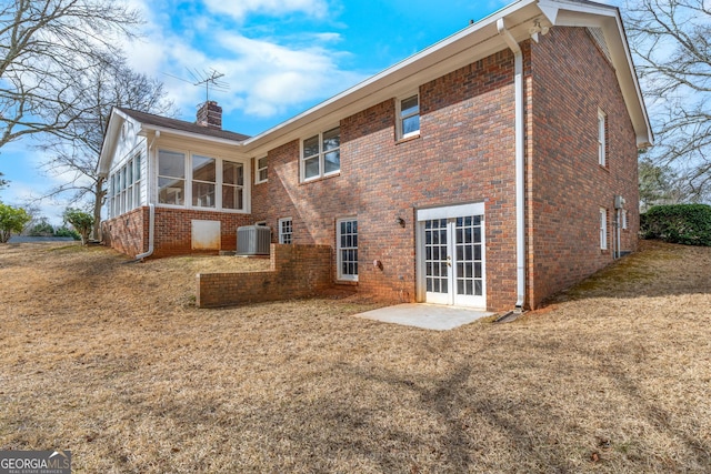 back of property with a sunroom, a chimney, french doors, central air condition unit, and brick siding