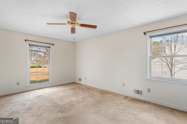 carpeted spare room with a healthy amount of sunlight, visible vents, a textured ceiling, and baseboards