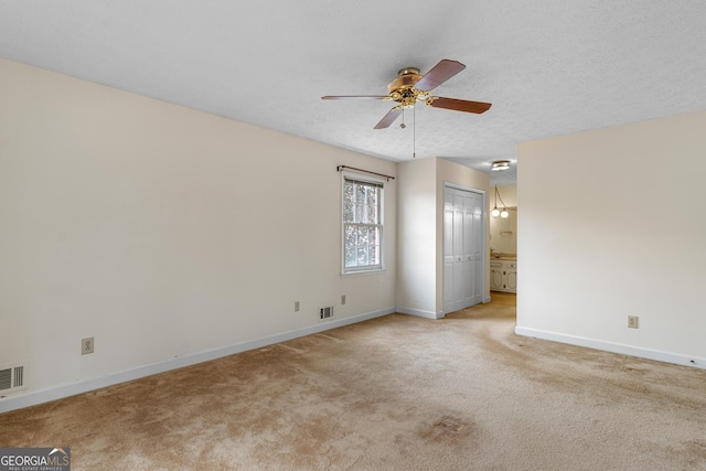 unfurnished room featuring ceiling fan, a textured ceiling, light colored carpet, visible vents, and baseboards