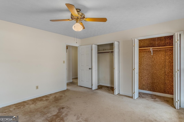 unfurnished bedroom featuring light carpet, a textured ceiling, two closets, and baseboards