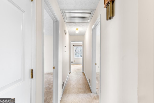 hallway featuring visible vents, light carpet, a textured ceiling, and baseboards