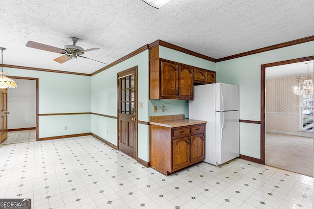 kitchen with a textured ceiling, ornamental molding, wainscoting, freestanding refrigerator, and light floors