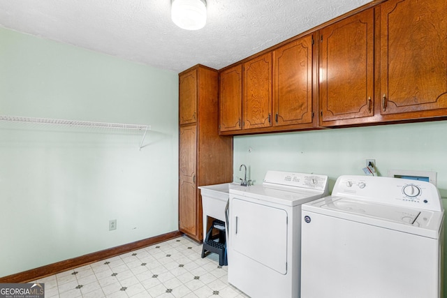 laundry area featuring light floors, washing machine and clothes dryer, cabinet space, a textured ceiling, and baseboards