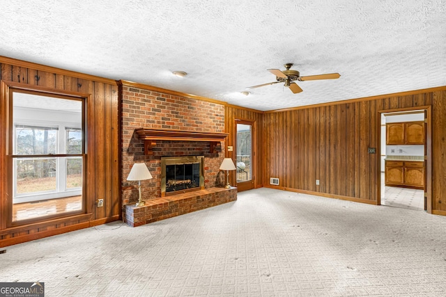 unfurnished living room featuring a textured ceiling, wooden walls, baseboards, a brick fireplace, and crown molding